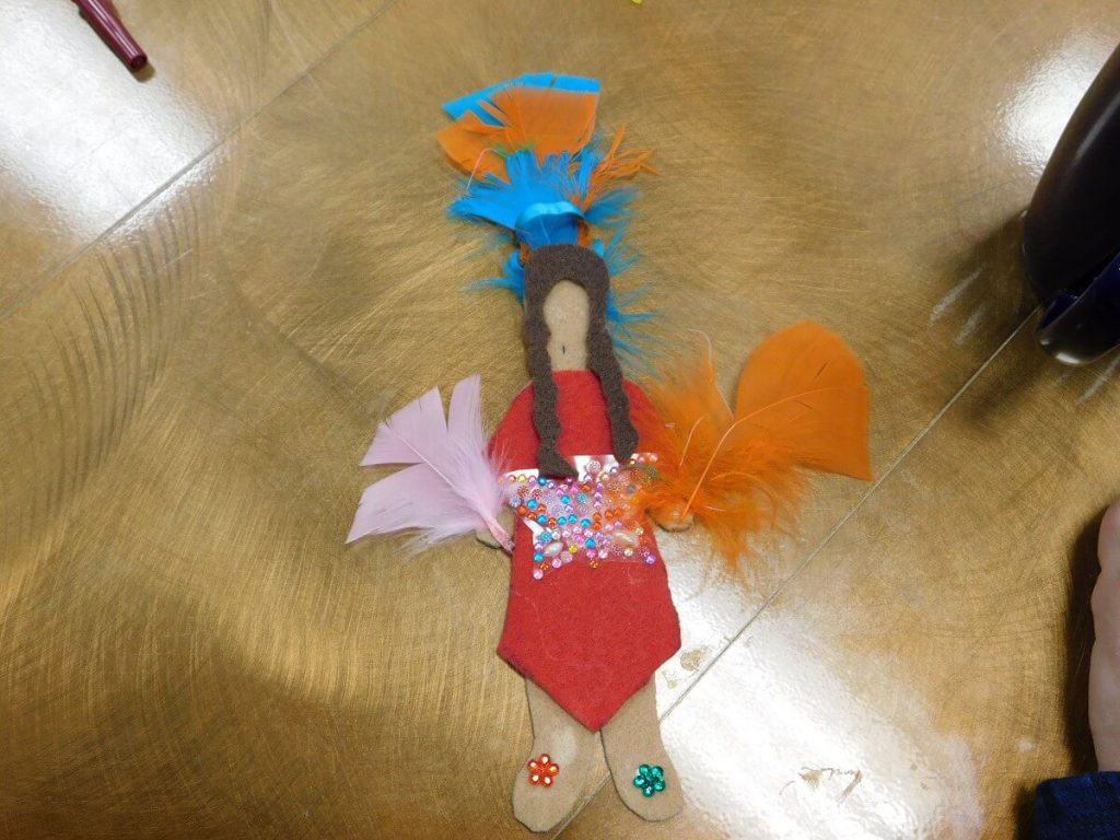 felt doll in a red dress holding feathers and feathers on head