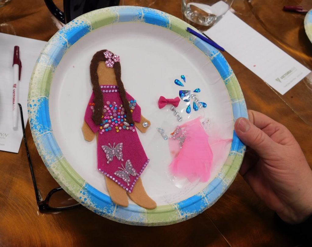 felt doll on plate with pink beaded dress, jewels on plate beside her