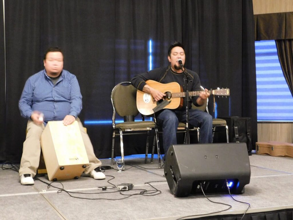 performer on stage playing guitar, another person holding amp