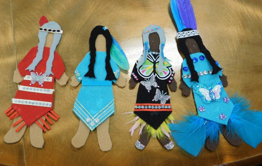 four felt dolls from left to right: doll in red dress, doll in blue dress, doll in black with butterflies, and doll in blue with butterflies and feathers